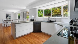 A modern kitchen with white cabinetry, a dishwasher, a sink, and a window with a view of greenery. - "Salt & Serenity" – close to Beach & Shops (Terrigal)