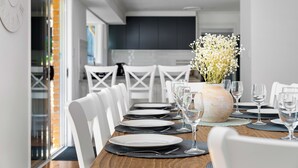 A dining table set with white chairs, plates, and wine glasses, with a vase of flowers in the center. - "Salt & Serenity" – close to Beach & Shops (Terrigal)