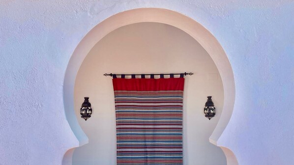 An arched doorway with a striped curtain and two wall-mounted lanterns.