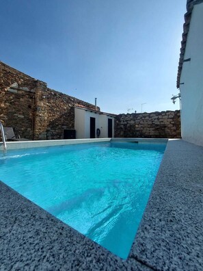 A swimming pool with stone walls and a small building with two doors.