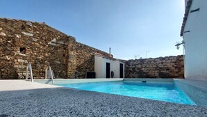 Une piscine aux murs en pierre et un petit bâtiment doté d’une porte.