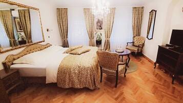 A hotel room with a large bed, a sitting area with a chair and a small table, a television, and a mirror.