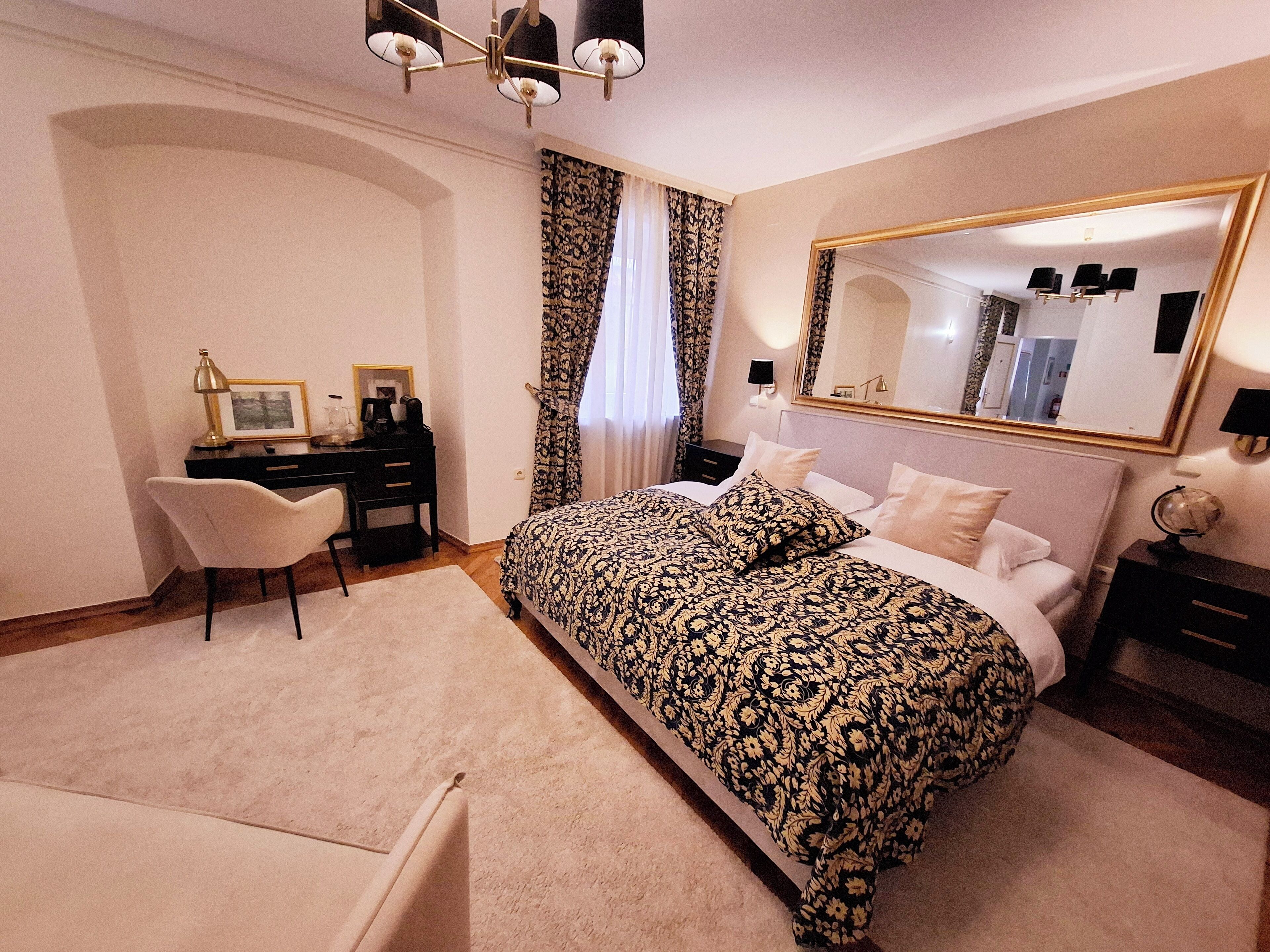 A bedroom with a large bed, a desk, a chair, a dresser, and a mirror.