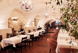 Un restaurante con mesas largas, techos abovedados y candelabros colgantes.