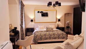 Een moderne slaapkamer met een groot bed, een bureau en een stoel. Er is een spiegel boven het bed en een kroonluchter.
