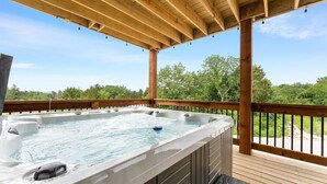 Ein Whirlpool auf einer Holzterrasse mit Blick auf Bäume und einen klaren Himmel.