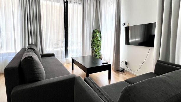 Uma sala de estar moderna com um sofá preto, uma mesinha e uma TV fixada na parede.