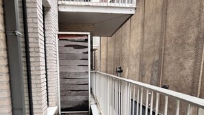 Um corredor estreito e fechado com corrimão de metal, parede de tijolo de um lado e parede de concreto do outro.