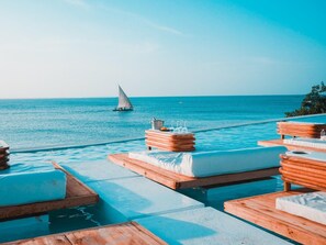 A poolside area with wooden loungers and a sailboat in the background. - Le Saint Tropez (Kidoti)