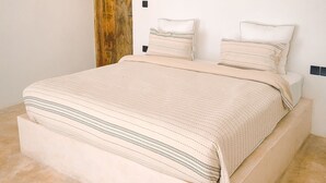 A minimalist bedroom with a large bed, a wooden door, and a plain white wall. - Le Saint Tropez (Kidoti)
