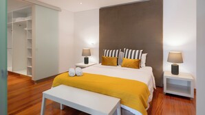 A modern bedroom with a large bed, bedside tables, a bench, and a walk-in closet.