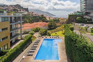 Una piscina con lettini, immersa nel verde e con vista su una cittadina costiera.