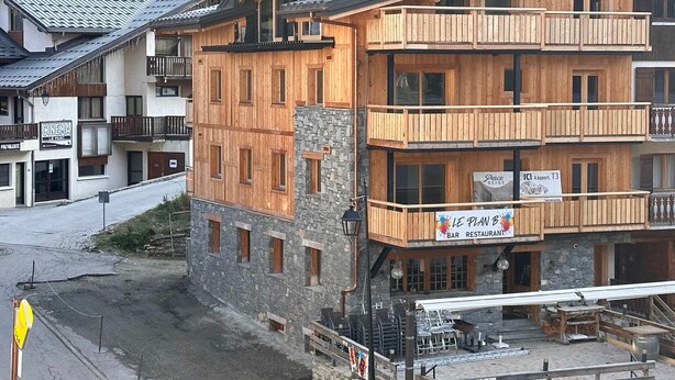 A multi-story wooden building with balconies, a stone base, and a sign for a bar and restaurant.
