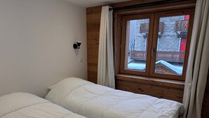 A bedroom with two beds, a window with curtains, and a wooden wall.
