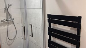 A bathroom with a glass shower enclosure, a black towel rack, and a white tiled wall.