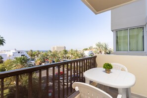 A balcony with a white table and chairs, a small potted plant, and a view of the sea and palm trees. - Great sea view apt in Las Américas (Playa de Las Americas)