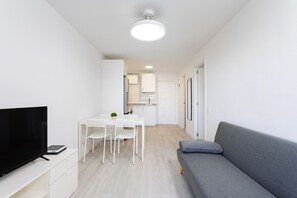 A modern, compact living space with a flat-screen TV, a dining table with chairs, a grey sofa, and a kitchen area in the background. - Great sea view apt in Las Américas (Playa de Las Americas)