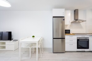 A modern kitchen with white cabinetry, a stainless steel refrigerator, an oven, and a dining area with a white table and chairs. - Great sea view apt in Las Américas (Playa de Las Americas)