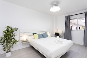 Ein modernes Hotelzimmer mit einem großen Bett, Nachttischlampen, einem Schreibtisch und einer Topfpflanze.