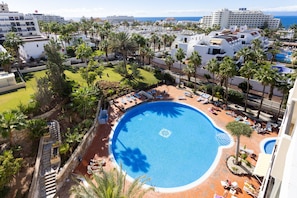 Ein Resort mit großem zentralen Pool, Palmen und Blick auf den Ozean.