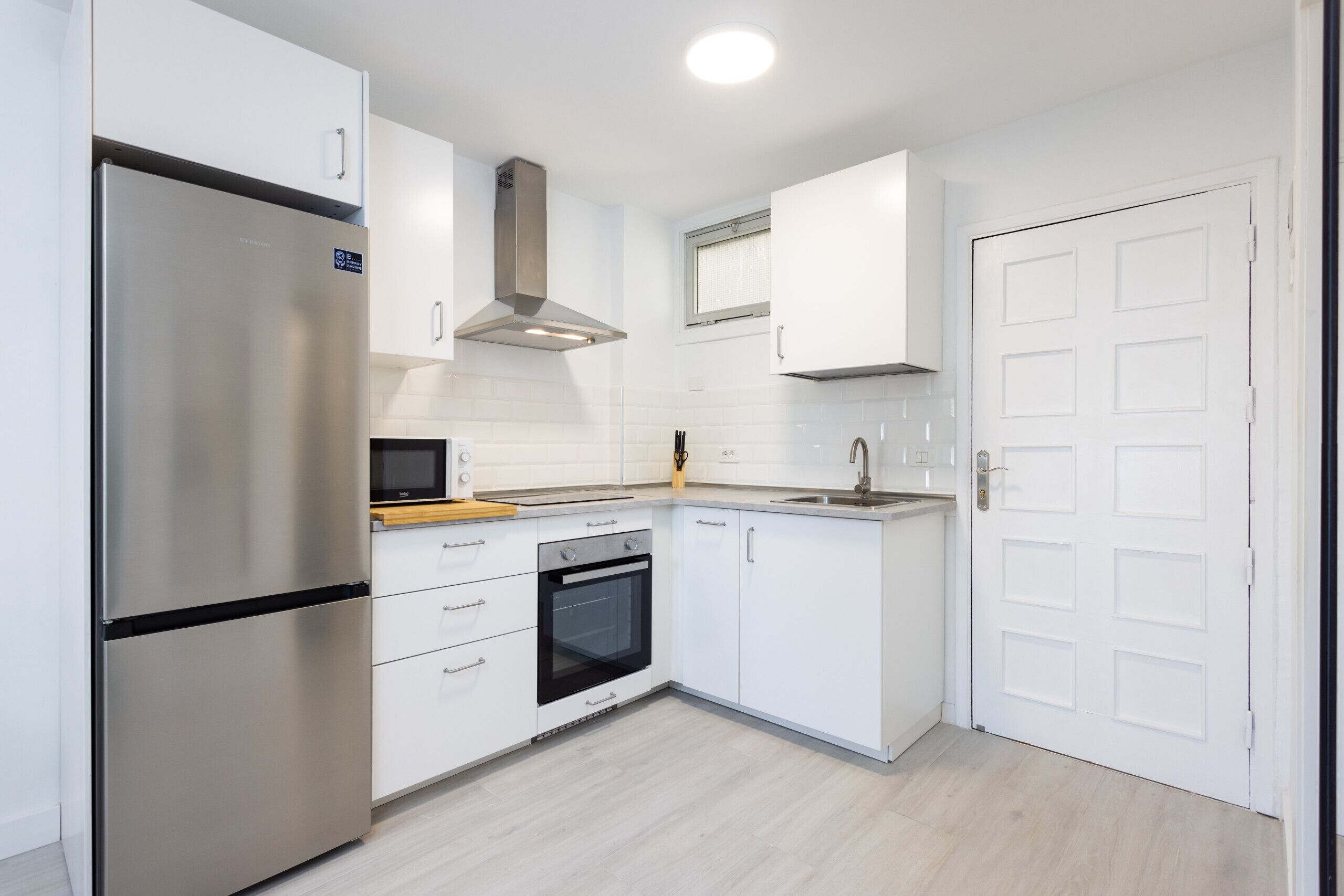 Een moderne keuken met witte kastjes, een roestvrijstalen koelkast, een ingebouwde oven en een magnetron.