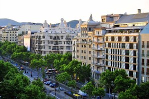A multi-story building with balconies, a street with cars, and trees.
