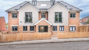 Et toetagers hus med murstensfacade, flere vinduer og et træhegn.
