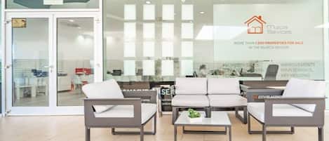A modern office space with a reception area, seating arrangement, and a glass door entrance.