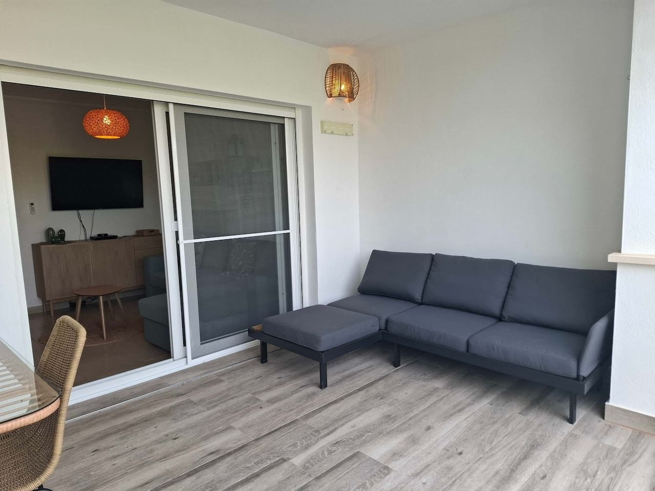 Una sala de estar moderna con un sofá gris, un pequeño reposapiés y un comedor con una mesa y sillas.