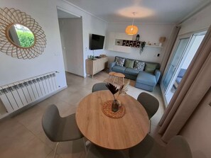 Un salon moderne avec une table à manger ronde en bois, un canapé et un téléviseur fixé au mur.