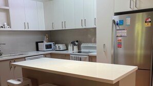 A modern kitchen with white cabinets, a central island with stools, a stainless steel refrigerator, and a microwave. - Newly renovated, 3 bedroom, pet friendly unit. (Lorne)