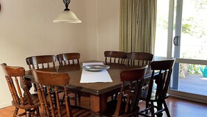 A dining area with a wooden table and chairs, a hanging light fixture, and a view of the outdoors through a sliding glass door. - Newly renovated, 3 bedroom, pet friendly unit. (Lorne)