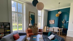 A living room with two sofas, a coffee table, and a dining area with a table and chairs. - Spacious family home near Orleans, quiet with garden (Loury)