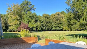 A wooden deck with a table and chairs, surrounded by a grassy lawn and trees. - Spacious family home near Orleans, quiet with garden (Loury)