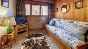 Tunnelmallinen mökin sisustus, jossa on puinen katto, kukkapintainen sohva, puinen televisioteline ja televisio sekä patteri.