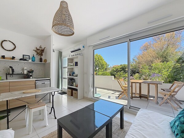 Une cuisine moderne avec des meubles blancs, un coin repas doté d’une table en verre et un balcon avec des chaises.