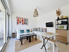 Un salon moderne comprenant un canapé, une table à manger, un téléviseur et un coin cuisine avec un four à micro-ondes.