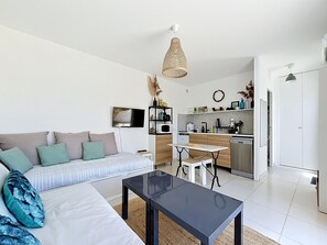 A modern living room with a sofa, a coffee table, a TV, and a kitchen area with a microwave, stove, and cabinets. - Studio with terrace and air conditioning, close to the beach (Mauguio)