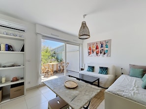 A modern living room with a sofa, a dining table, and a kitchen area with shelves and a refrigerator. - Studio with terrace and air conditioning, close to the beach (Mauguio)