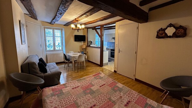Et hyggeligt rum med en seng, sofa, spisebord og et køkken, der kan anes gennem en åben dør.