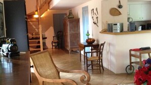 Una sala de estar acogedora con una silla de madera, una mesa de comedor con sillas, una zona de cocina con microondas y una escalera que sube a otro nivel.