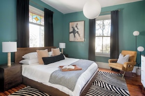 A bedroom with a large bed, two bedside tables with lamps, a chair, a zebra-patterned rug, and a stained glass window. - Casa Azula (Atlanta)