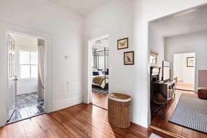 A hallway with wooden flooring, a wicker basket, and a bed with a striped bedspread in the background. - Casa Azula (Atlanta)