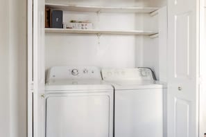 A laundry room with two white front-loading washing machines and a shelf above them. - Casa Azula (Atlanta)