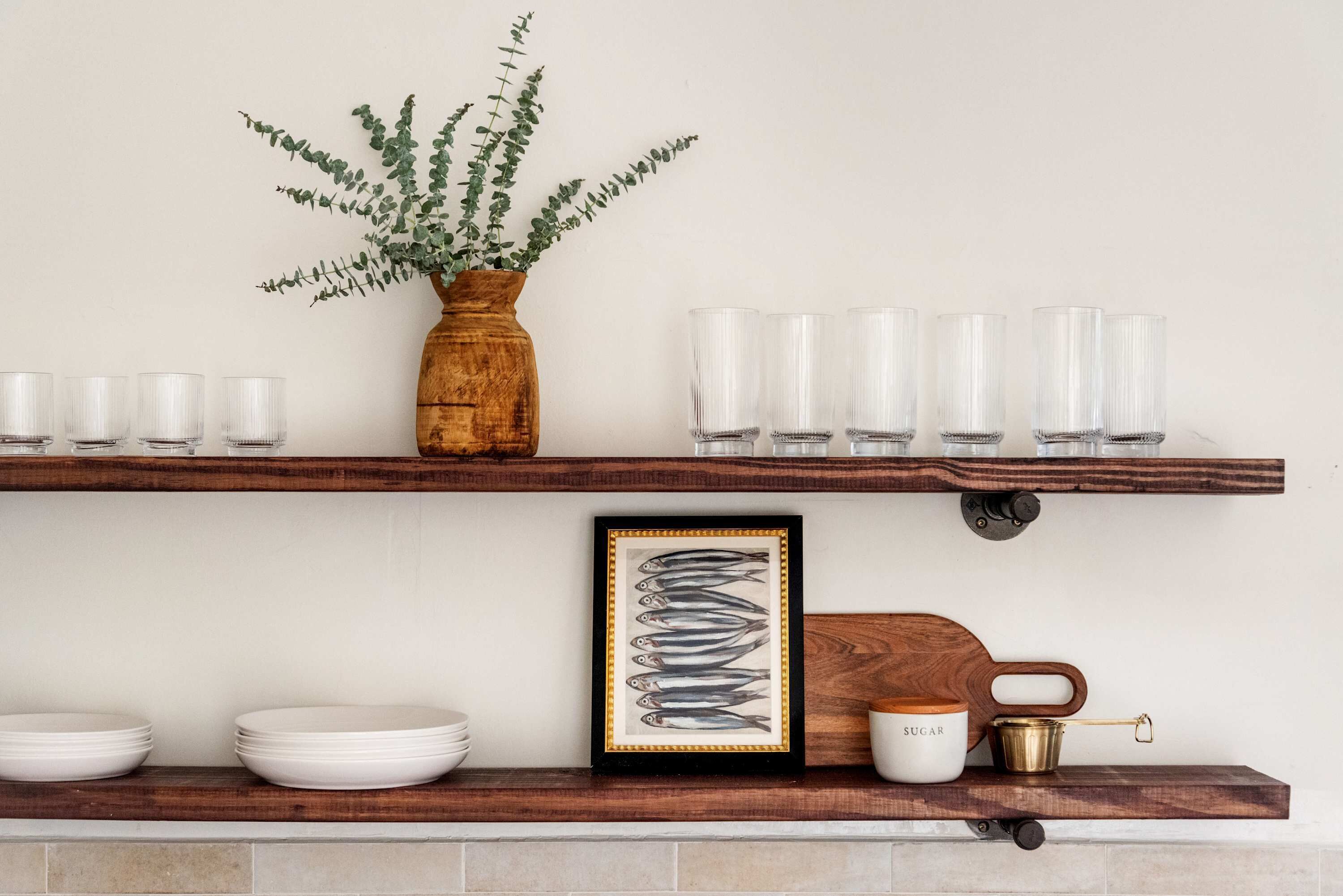 A kitchen shelf with glassware, a framed picture, and a plant.