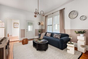 Un salon moderne avec un canapé bleu foncé, une table basse ronde ornée de livres, un tapis à motifs et un luminaire original.