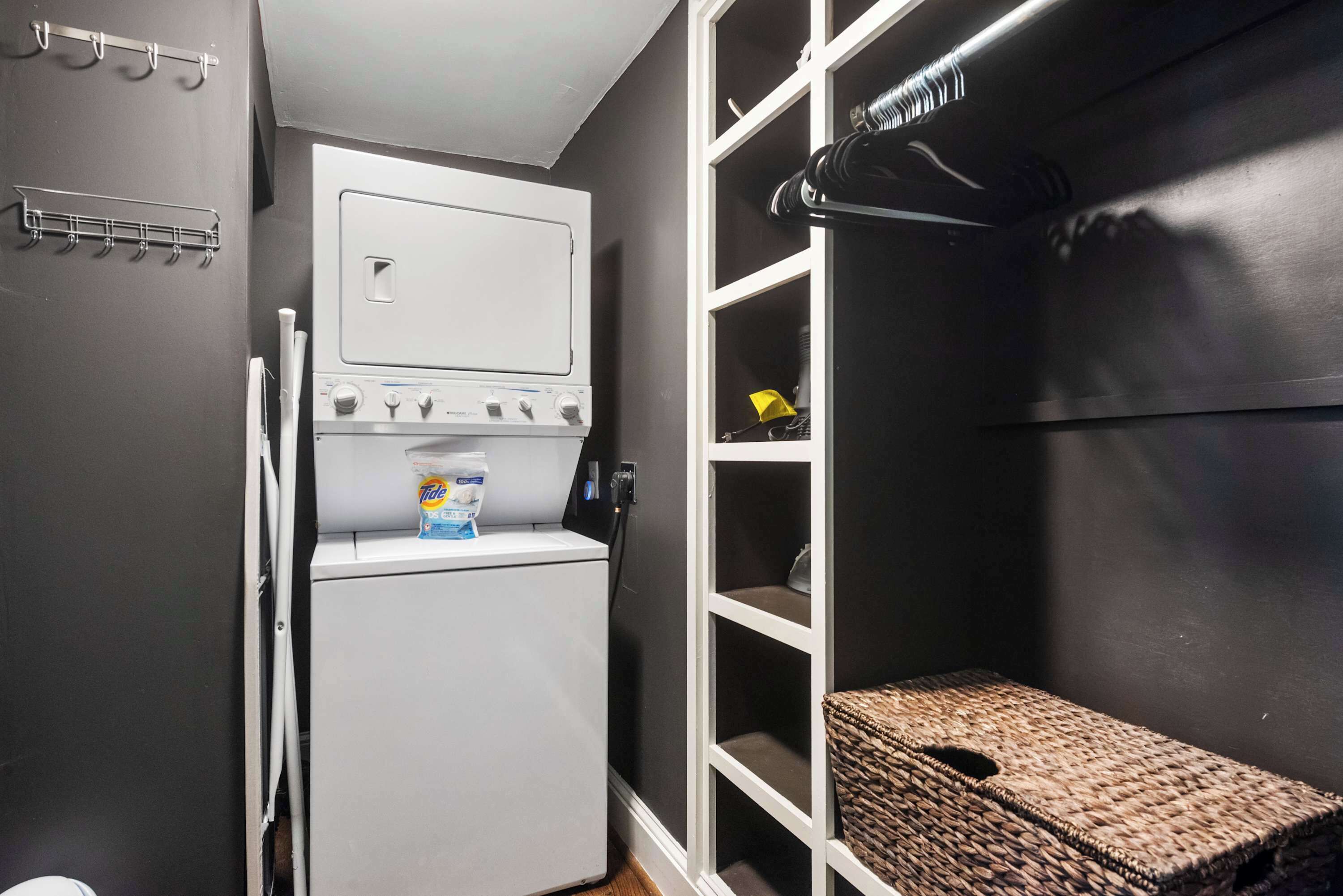 A compact laundry room with a white dryer, a small shelf with a detergent bottle, and a wicker basket on a shelf.
