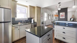 A modern kitchen with light-colored cabinets, a stainless steel refrigerator, a granite countertop, and a dining area with a chair and table. - Rustic Rouge (Atlanta)