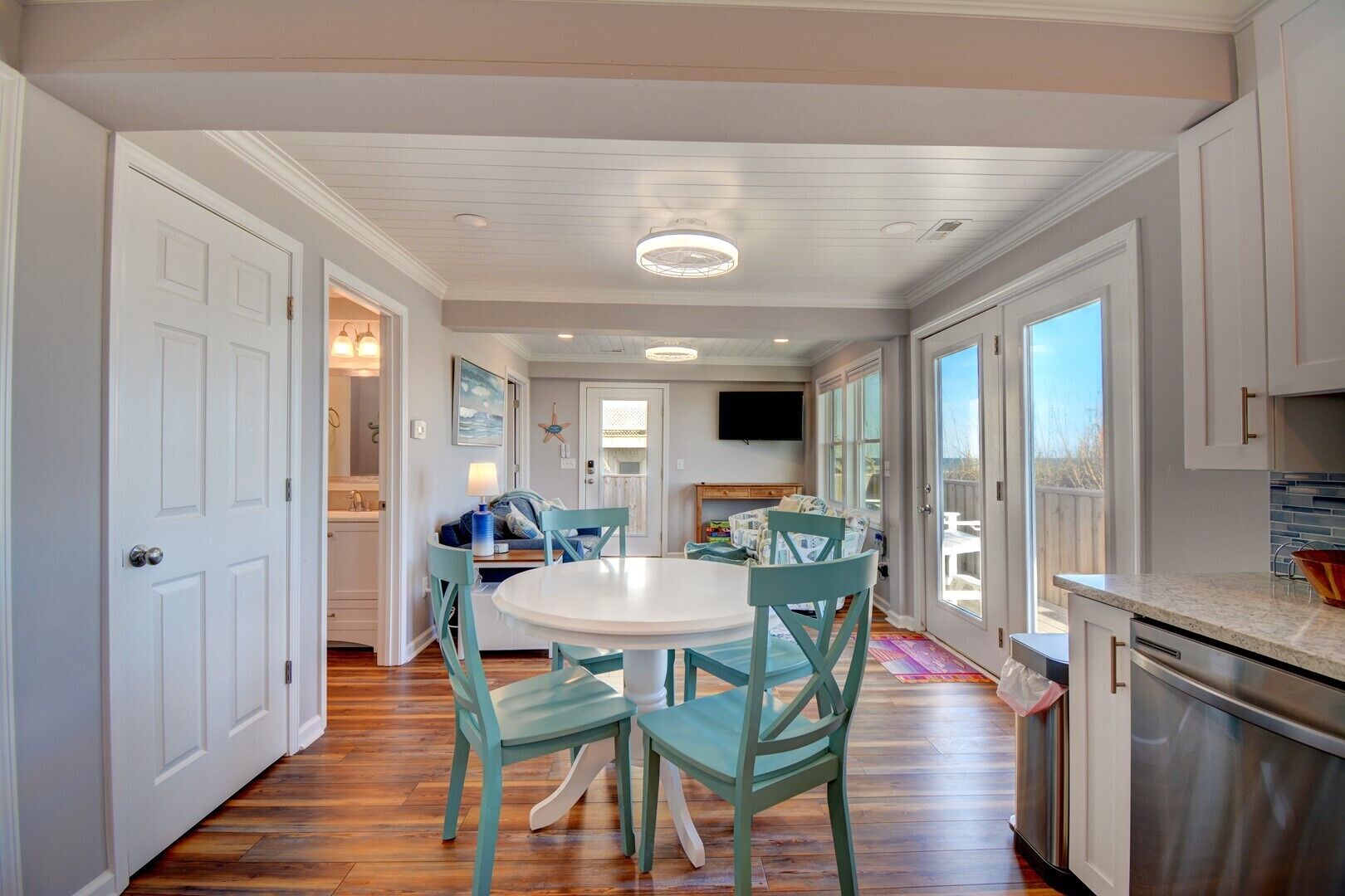A spacious kitchen with white cabinets, a dining area with teal chairs, and a large window providing a view of the outdoors.
