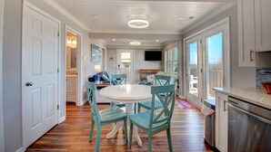 Una cocina amplia con armarios blancos, un comedor con sillas color turquesa y un ventanal con vistas al exterior.